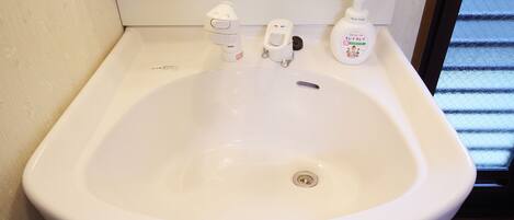 A white bathroom sink with a handheld soap dispenser and a bottle of hand soap.