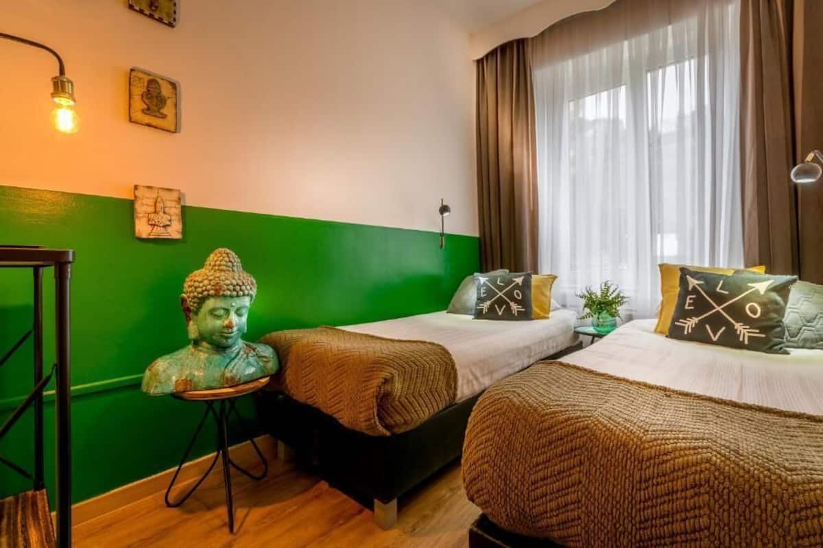 Une chambre avec deux lits, un mur d’accent de couleur verte et une statue de Bouddha.