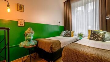 A room with two beds, a green accent wall, and a Buddha statue.