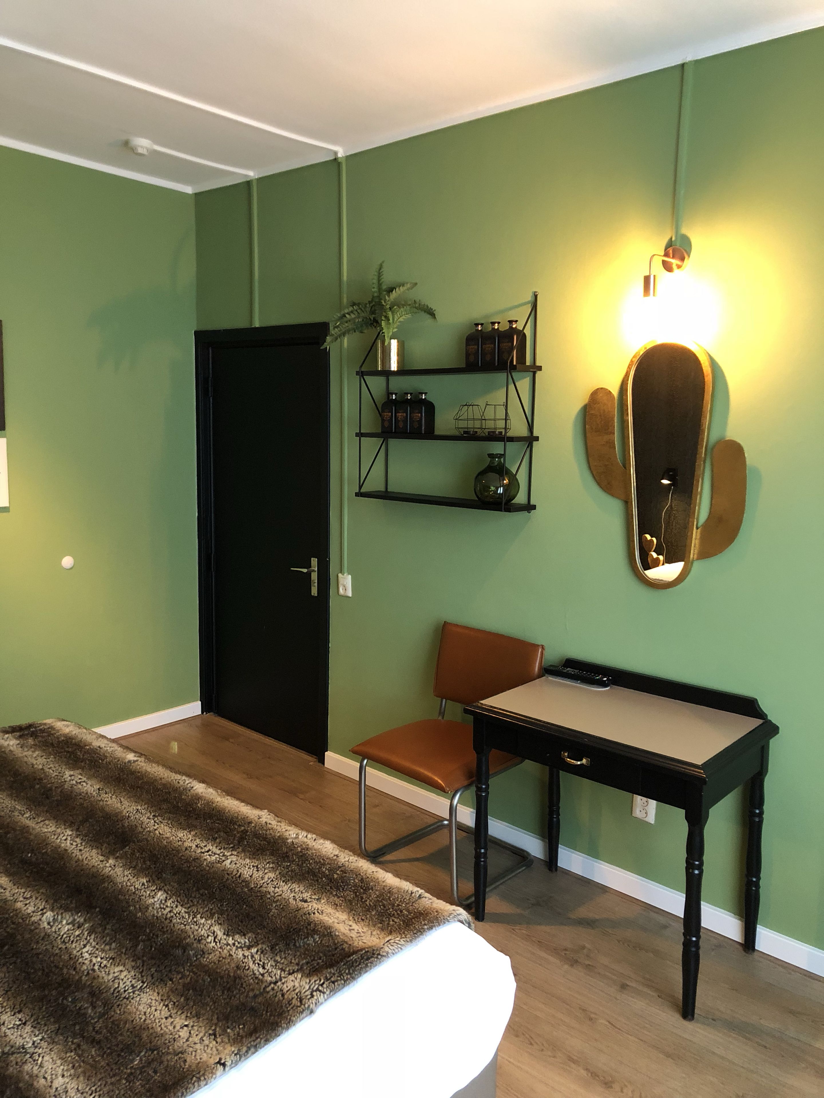 Una habitación con cama, escritorio, silla, estante con adornos y una puerta.
