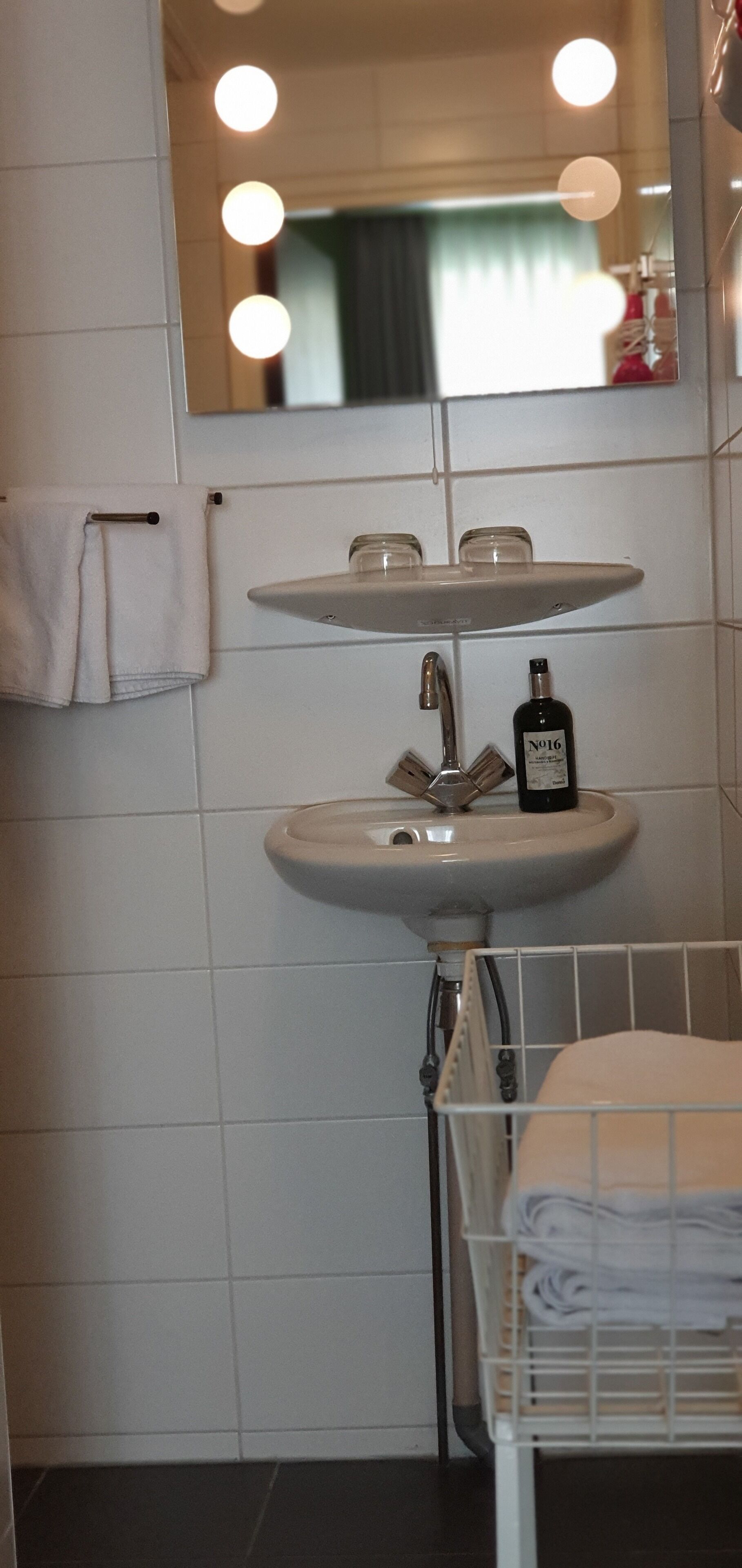 Ein Badezimmer mit einem Doppelwaschbecken, einem Handtuchhalter und einem beleuchteten Spiegel.
