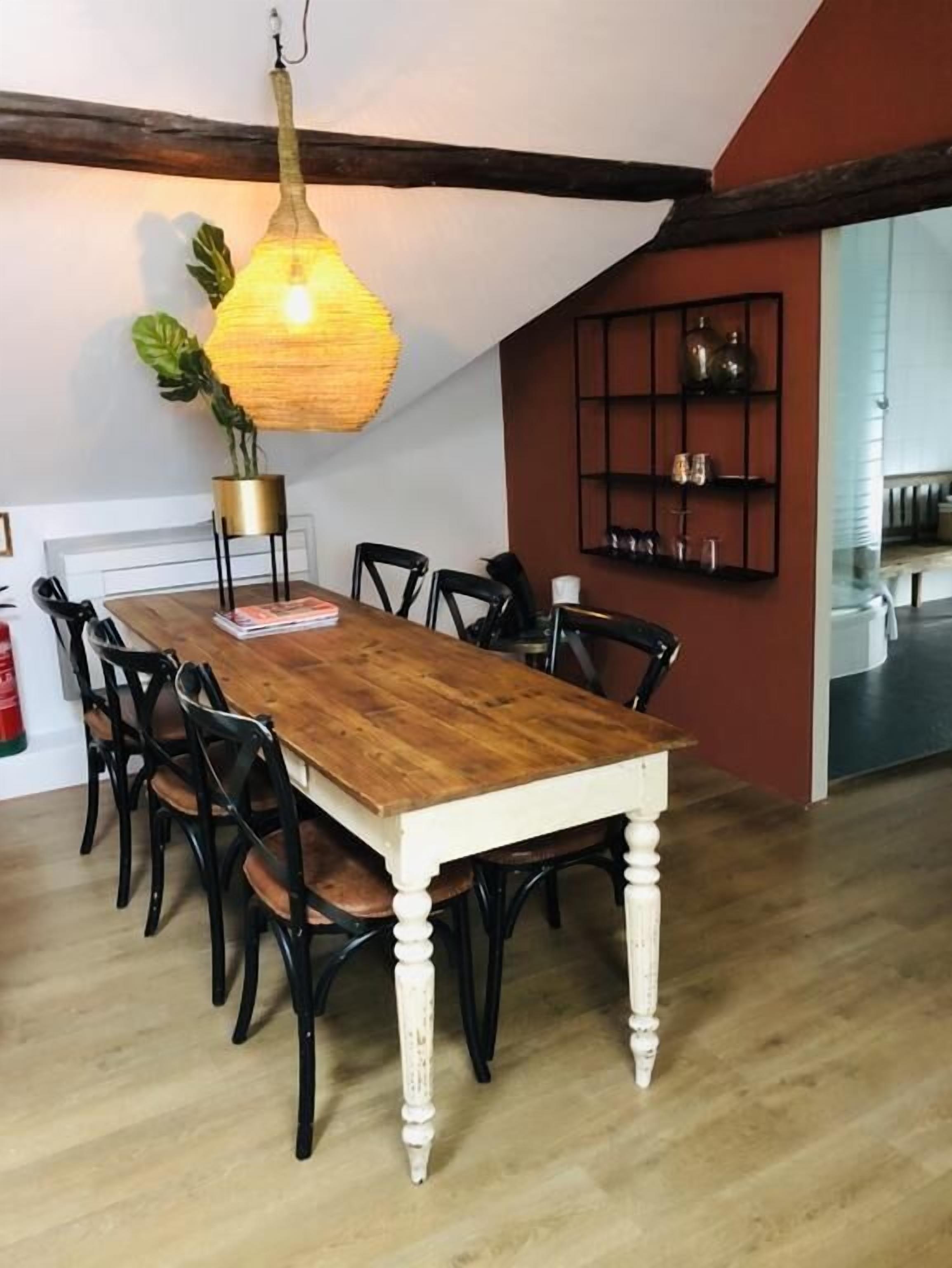 Comedor con mesa de madera, sillas negras, lámpara colgante y una planta.