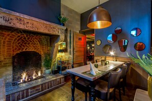 A cozy dining area with a brick fireplace, a table with chairs, and a hanging pendant light. - Hotel Valkenhof (Valkenburg aan de Geul)