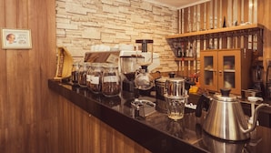 A kitchen with a stone backsplash, wooden cabinets, and a coffee station with a grinder, kettle, and jars of coffee beans. - Marrakesh Inn (Jakarta)