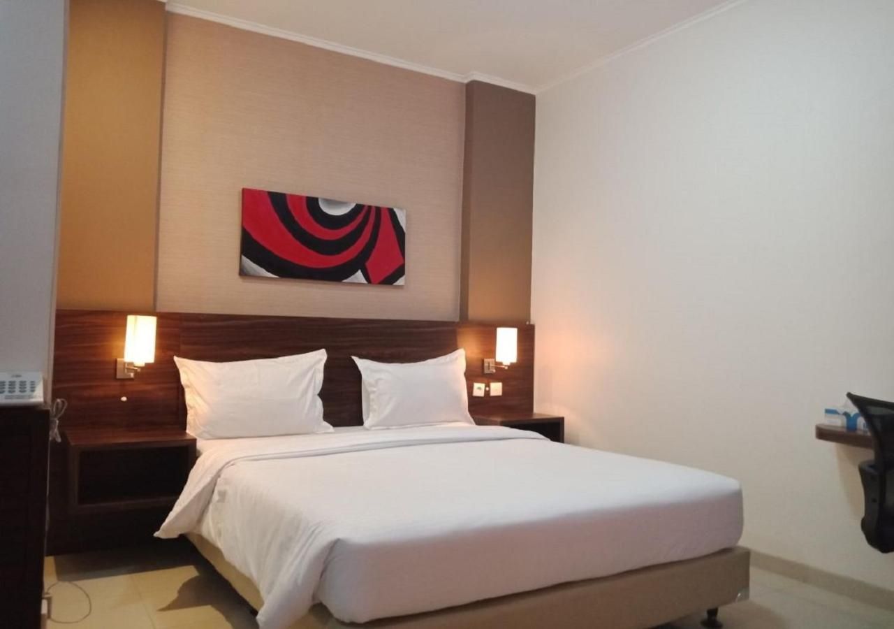 A hotel room with a bed, two bedside lamps, a wall-mounted artwork, and a wooden headboard.