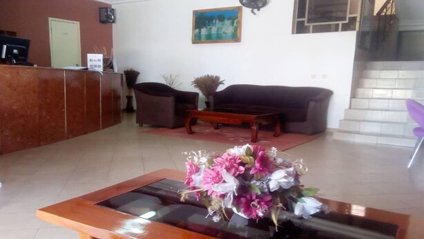 A reception area with a wooden reception desk, two brown sofas, a coffee table, and a floral arrangement on a glass table. - Hotel Aladje (Abidjan)
