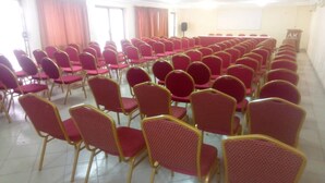 A conference room with rows of red chairs and tables, a podium, and a projector screen. - Hotel Aladje (Abidjan)
