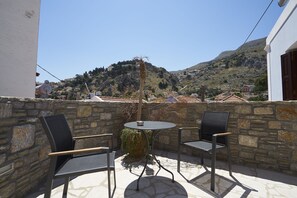A patio with two chairs and a table, overlooking a hillside with houses. - Kaminos Village (Symi)