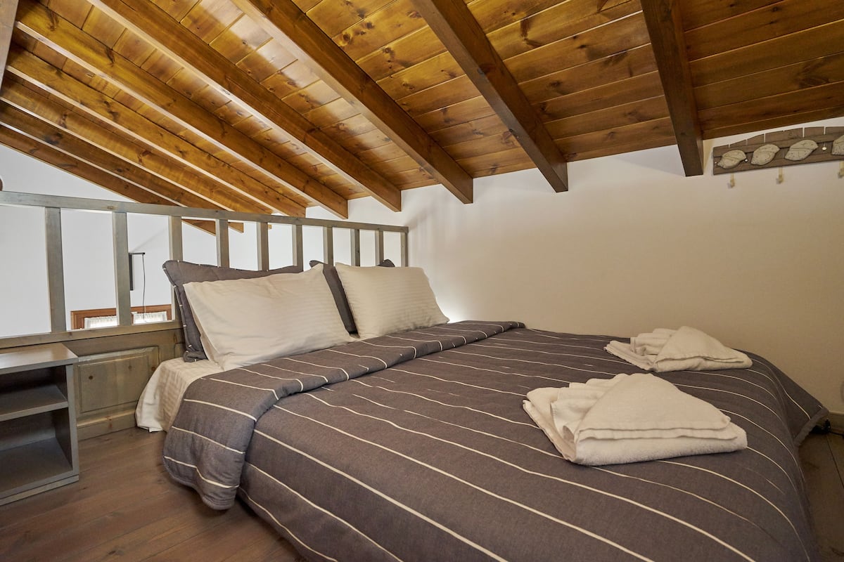 A bedroom with a wooden ceiling, a bed with striped bedding, and a window with a view.