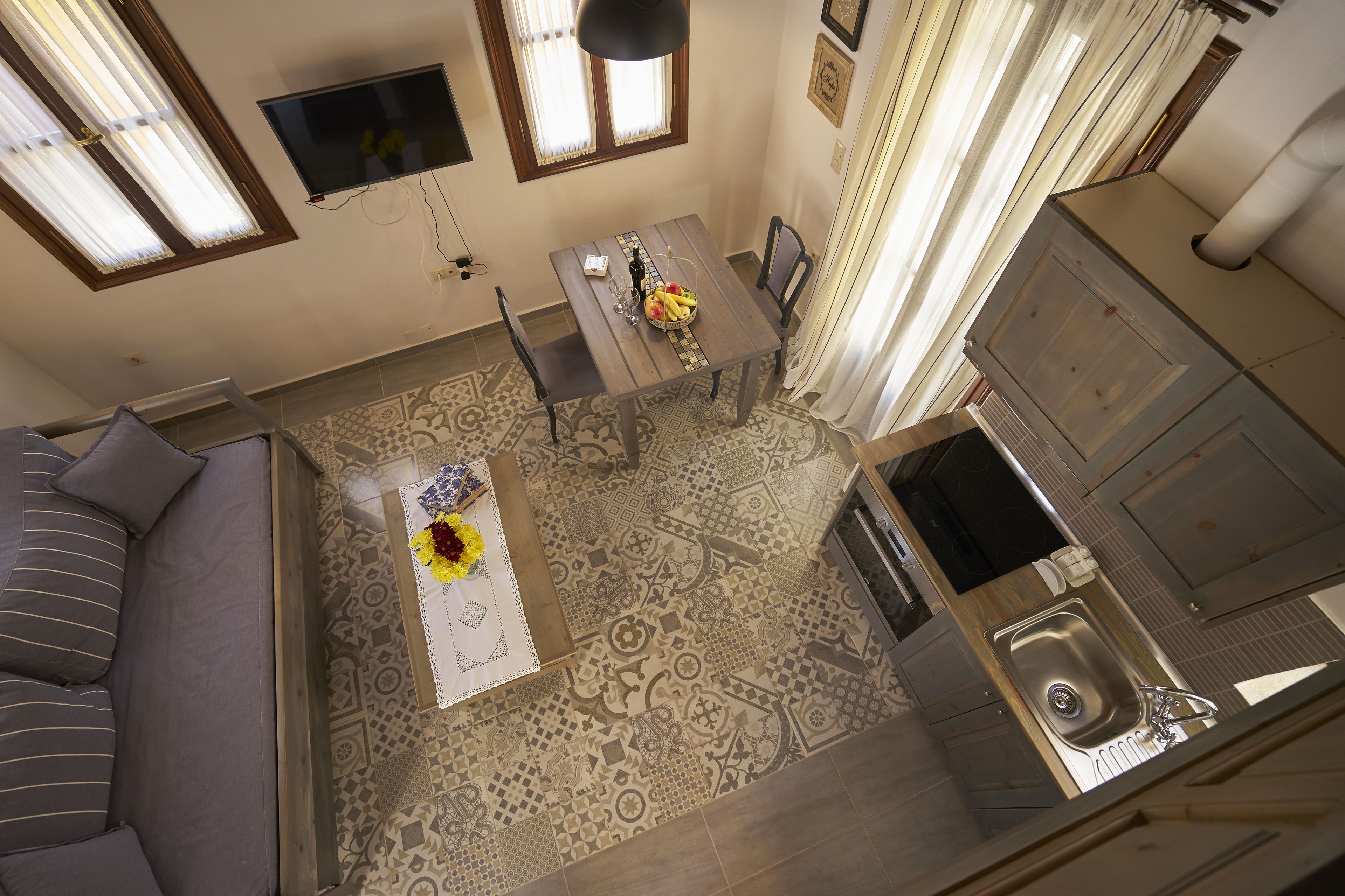 A compact living space with a sofa, a dining table with a vase of flowers, a kitchen area with a sink, and patterned flooring.