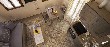 A compact living space with a sofa, a dining table with a vase of flowers, a kitchen area with a sink, and patterned flooring.