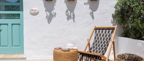 A white building with a turquoise door, three flower planters, a hammock, and a yellow cushion.