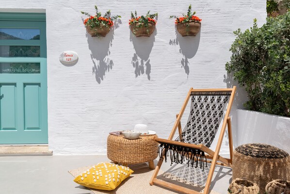 A white building with a turquoise door, three flower planters, a hammock, and a yellow cushion. - Kaminos Village (Symi)