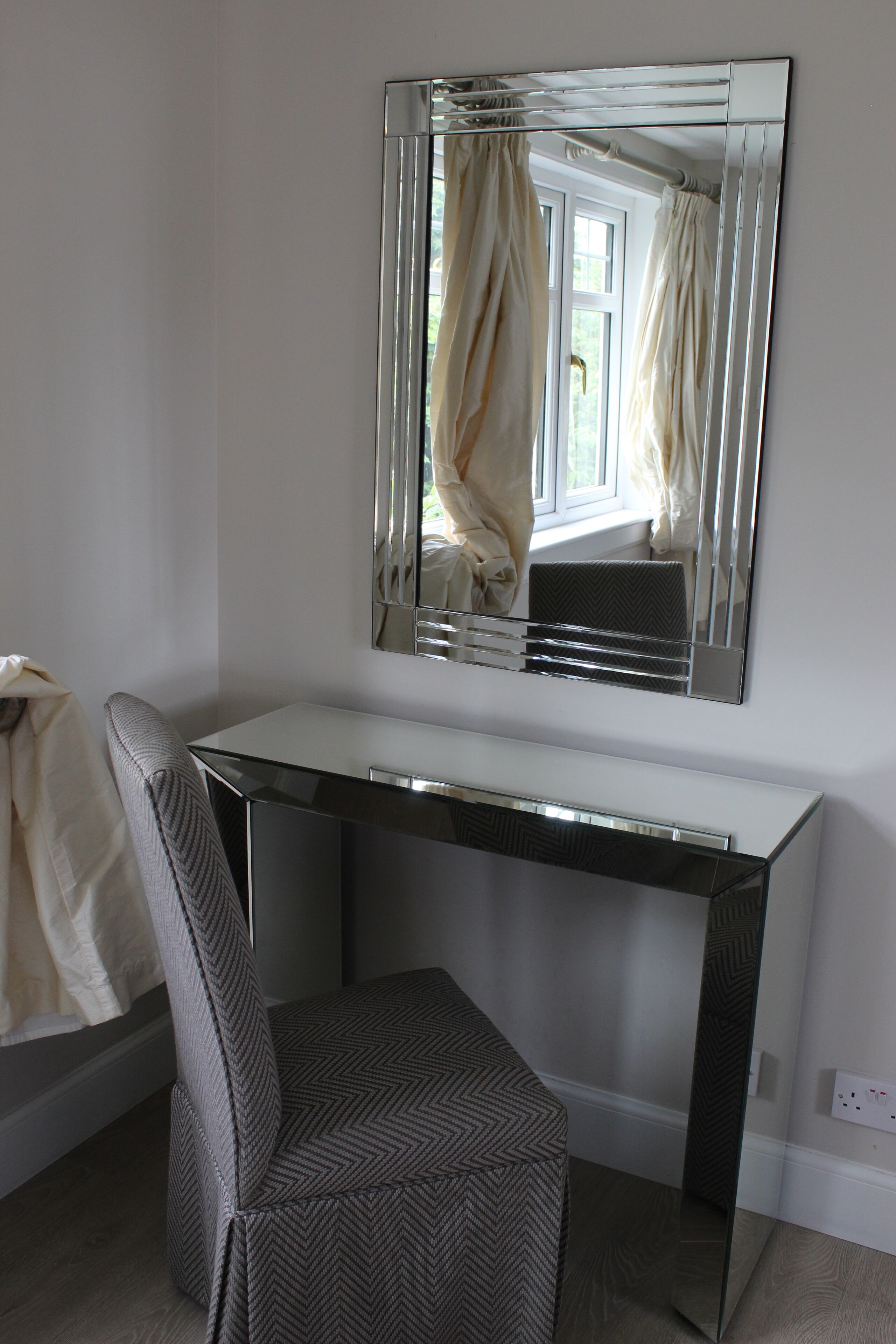 A modern room with a white desk, a chair, and a large mirror on the wall.