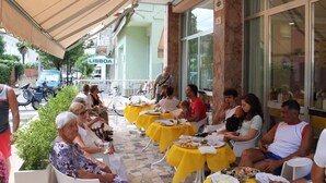 An outdoor dining area with yellow tables and chairs, a covered seating area, and a building with a sign reading "LISBOA". - Hotel Madrid (Cattolica)