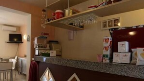 A hotel reception area with a counter, shelves with various items, a television, and a dining area with chairs and tables. - Hotel Madrid (Cattolica)
