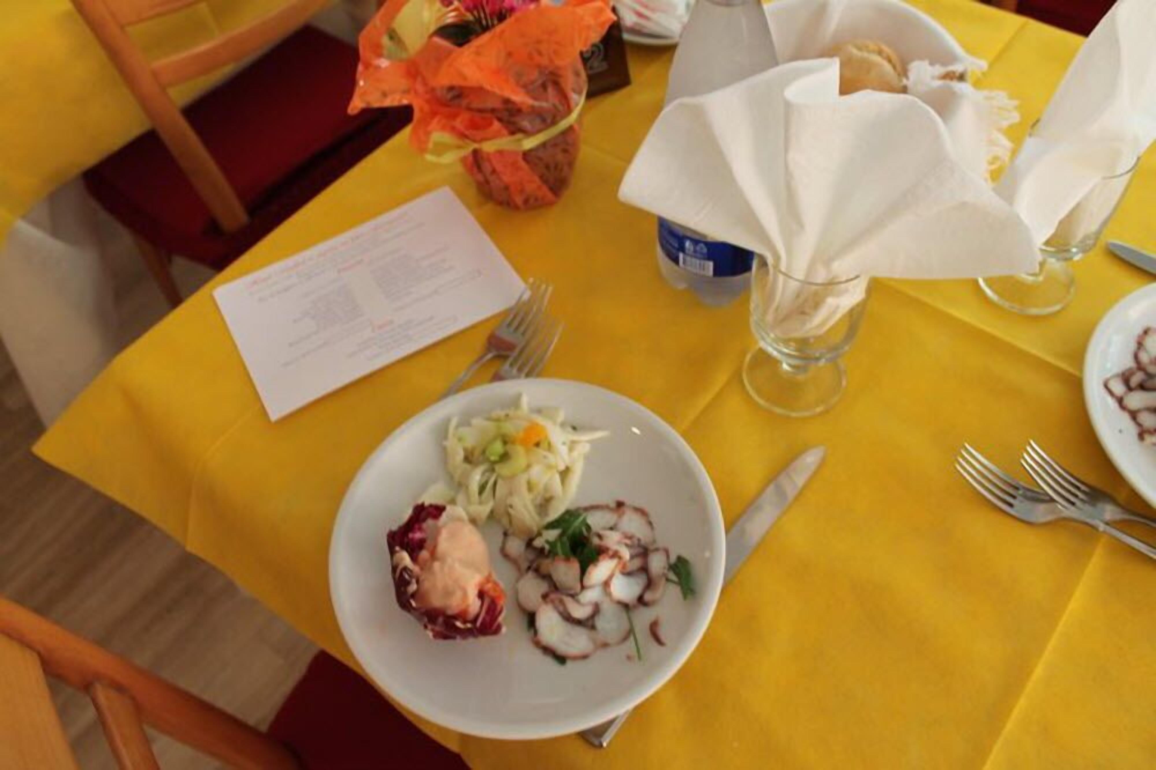 Un tavolo da pranzo con una tovaglia gialla, un piatto di cibo, una bottiglia e un menu.