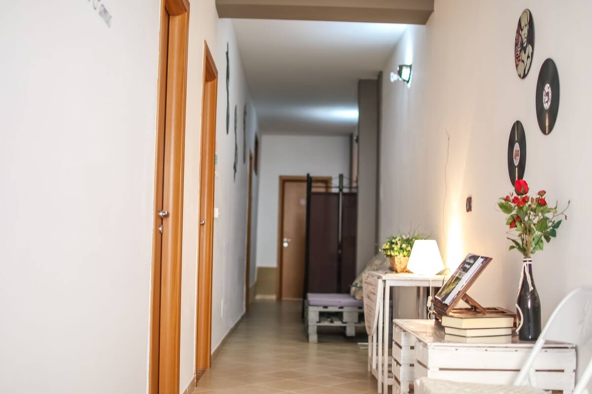 A hallway with a wooden door, a bench, a table with a lamp, and a vase with flowers.