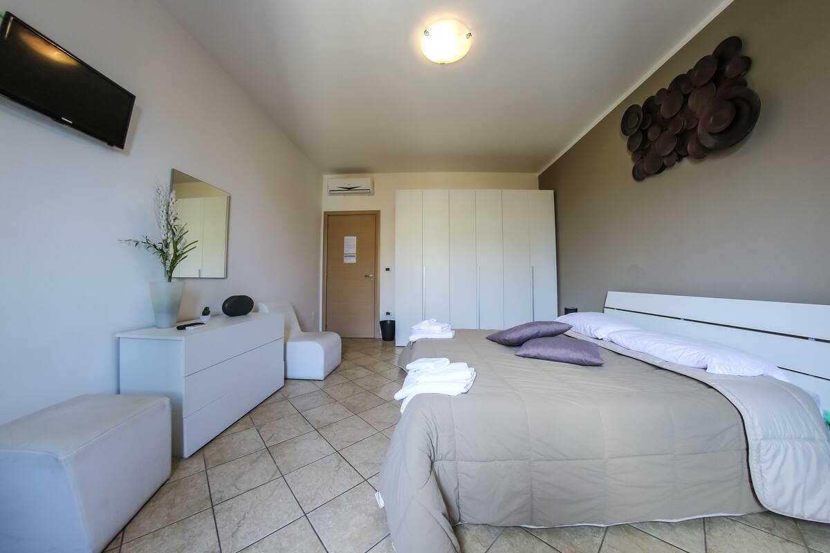 A modern hotel room with a bed, a dresser, a mirror, and a flat-screen TV.
