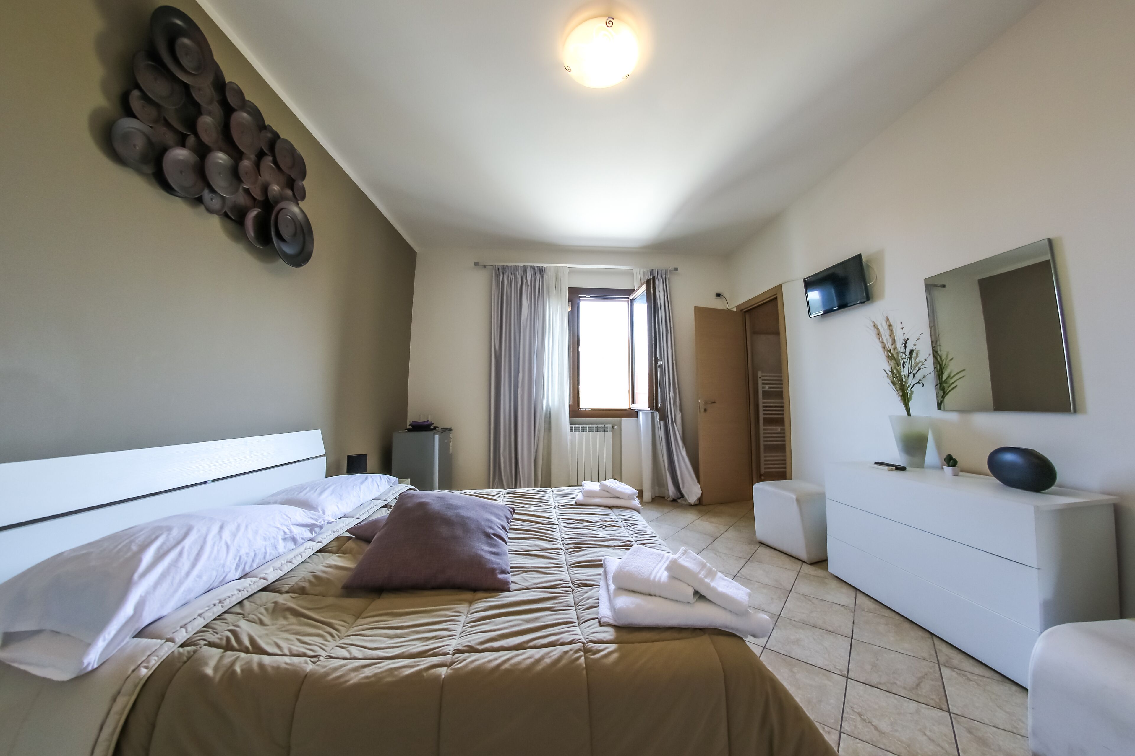A modern bedroom with a bed, a dresser, a TV, and a window with curtains.
