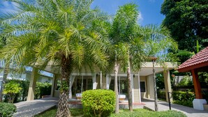 A building with a covered outdoor area, surrounded by lush greenery and palm trees. - Janthawong Bangtao House (Choeng Thale)