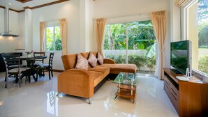A living room with a sofa, TV, glass coffee table, and a dining area with chairs and a table. - Janthawong Bangtao House (Choeng Thale)