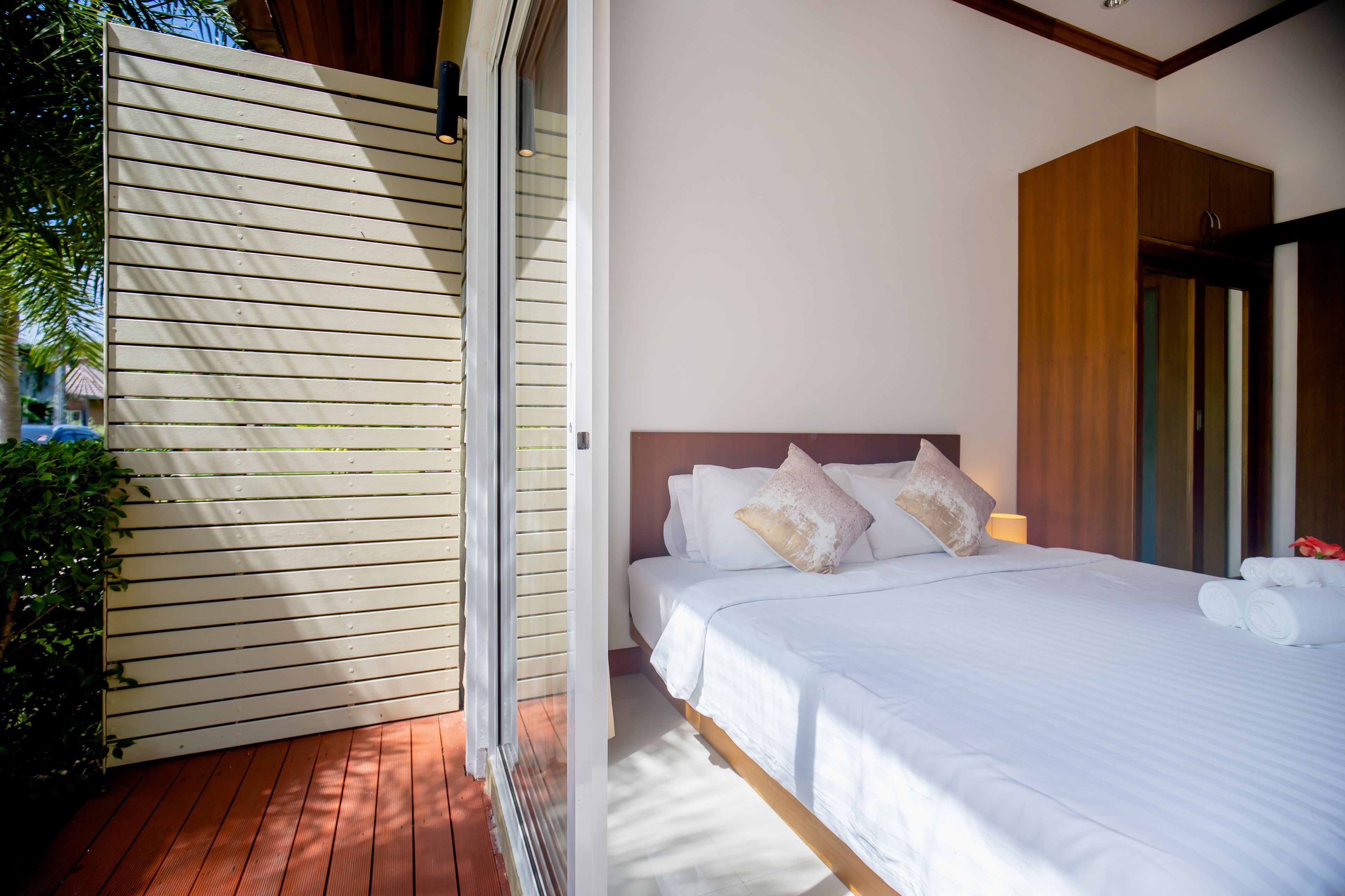 A bedroom with a wooden bed, white bedding, and a view of the outdoors.