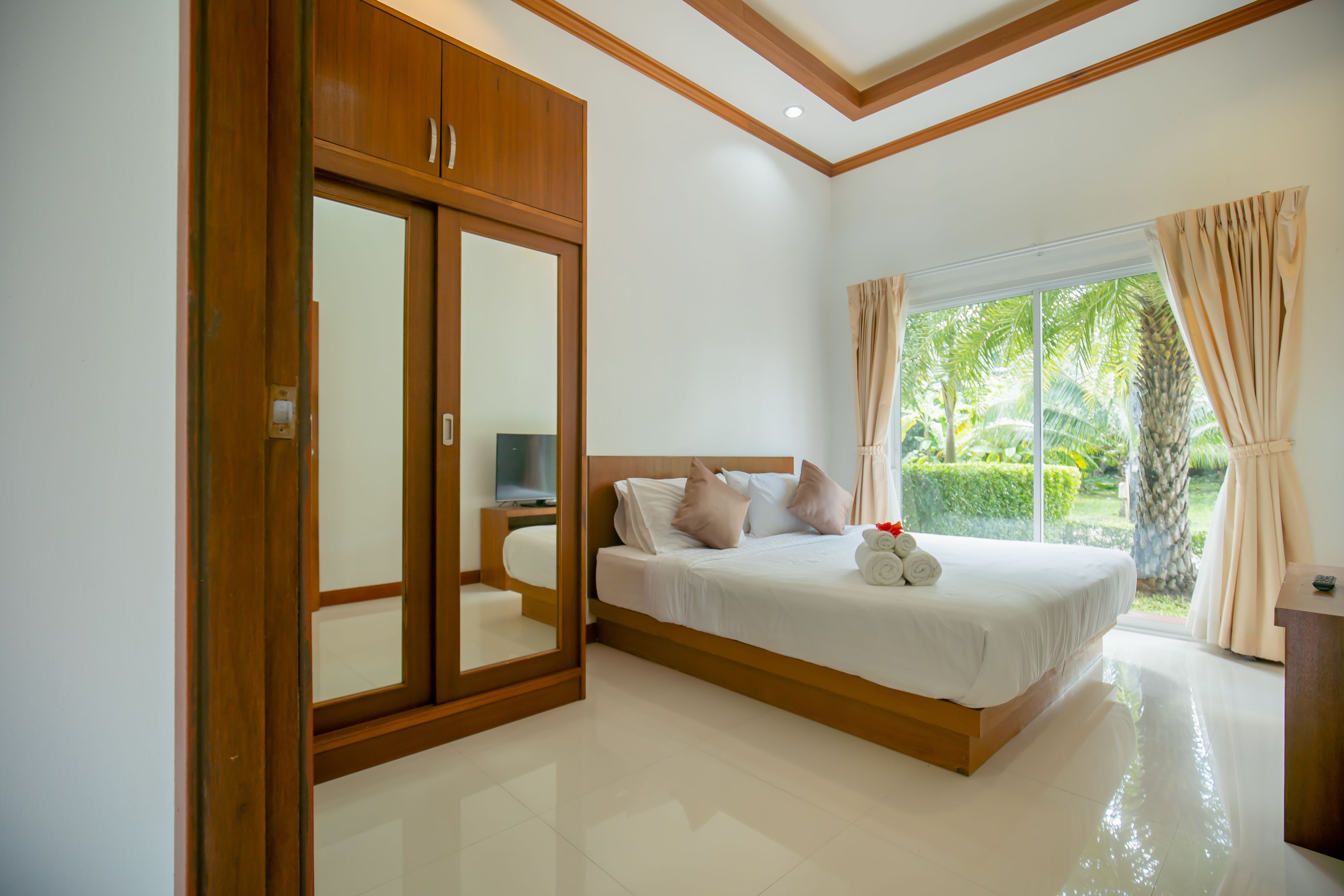 A bedroom with a large bed, a wardrobe, a TV, and a window with curtains.