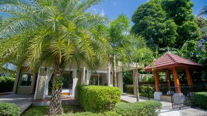 A building with a red-roofed gazebo, palm trees, and a well-maintained garden. - Janthawong Bangtao House (Choeng Thale)
