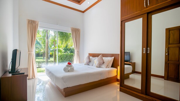 A modern bedroom with a large bed, a TV, and a wardrobe. - Janthawong Bangtao House (Choeng Thale)