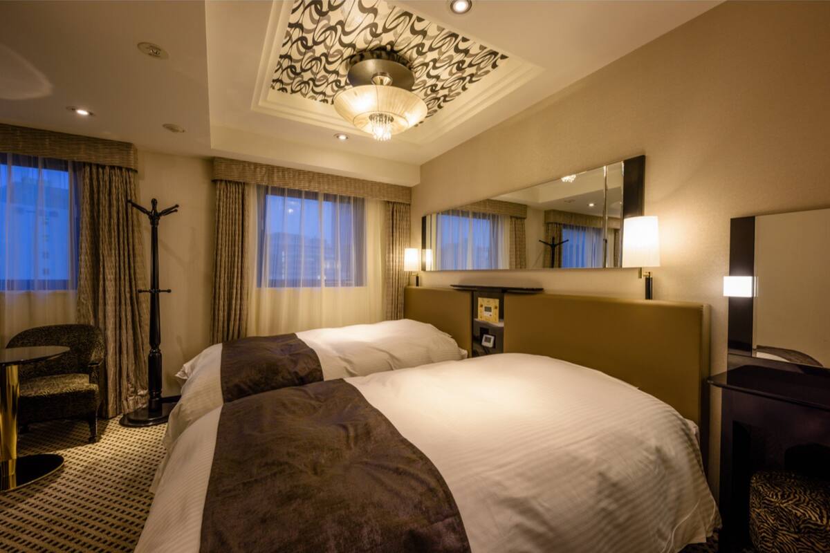 A hotel room with a large bed, a desk, a chair, a standing lamp, and a mirror.