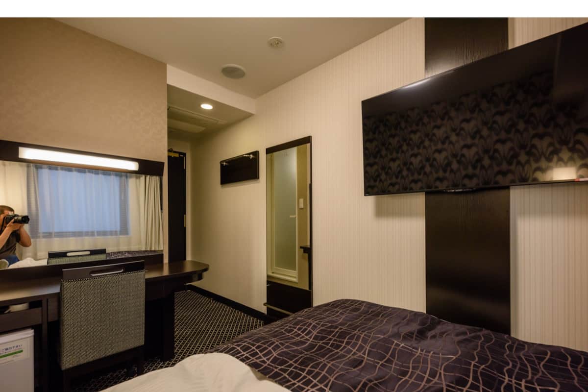 A hotel room with a bed, a desk, a mirror, and a wardrobe.