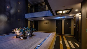 Een moderne hotellobby met een houten vloer, plantenpotten en een overzichtelijk pad aangegeven met pijlen.