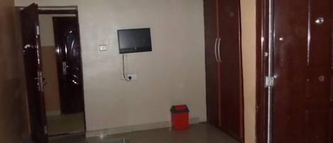 A room with a television mounted on the wall, a small table, a red trash bin, and a wardrobe.