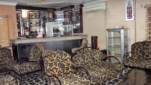 A bar area with patterned sofas and chairs, a counter with a refrigerator, and a Coca-Cola poster on the wall. - B & S Hotel (Lagos)