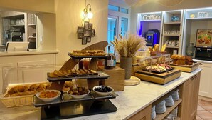 Montaje de bufé con diversos alimentos, una estación de café y un jarrón decorativo con plantas secas.