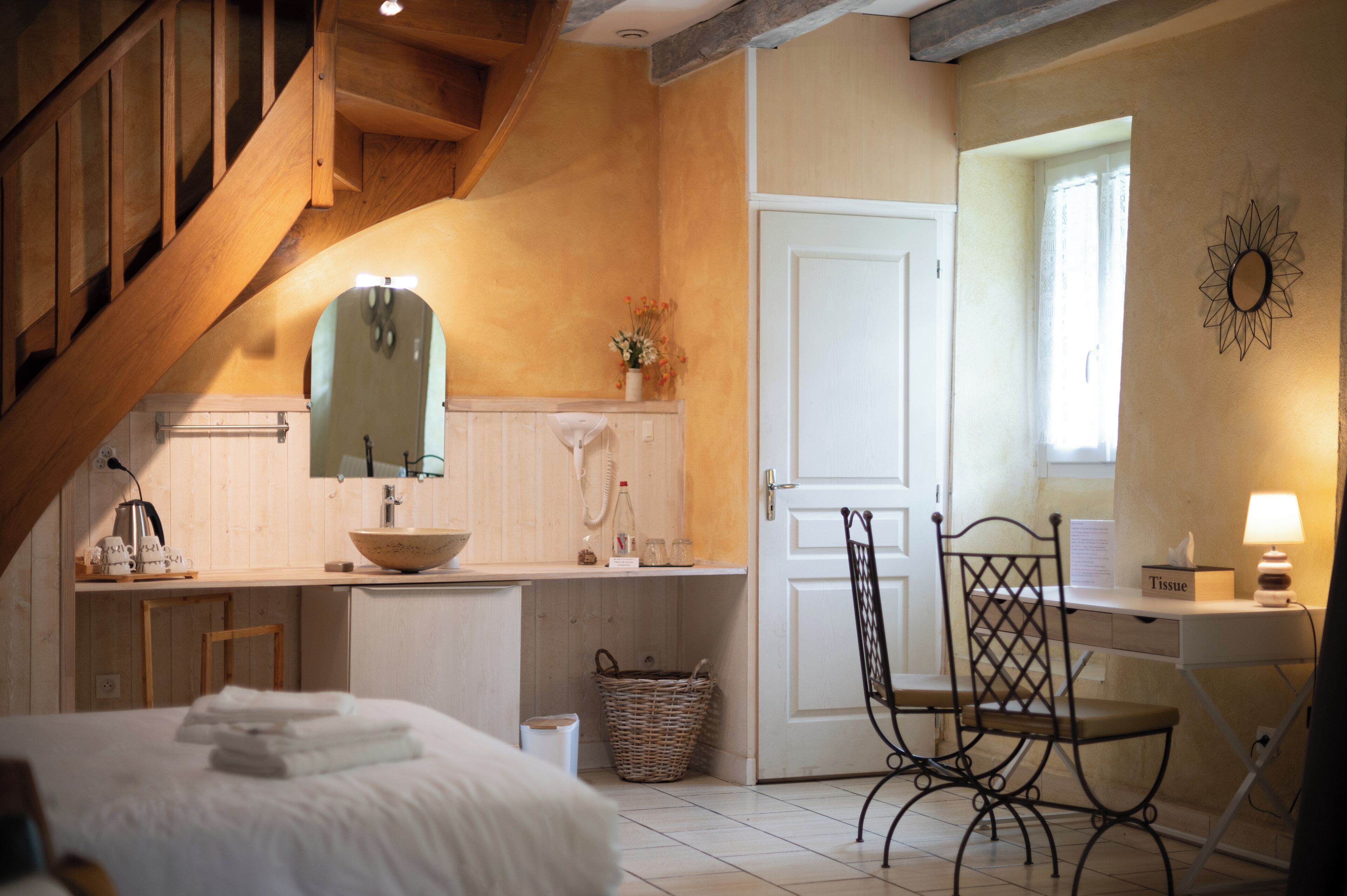 Une chambre confortable avec un escalier en bois, un grand lit recouvert de draps blancs, une table de chevet avec une lampe et un petit bureau avec une chaise.