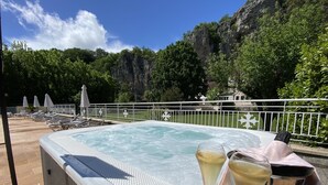 Un jacuzzi con sillones de descanso y sombrillas, rodeado por una valla blanca, con montañas al fondo.