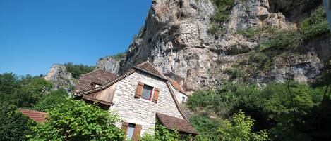 Un bâtiment en pierre, doté d’un toit en pente, adossé à une falaise rocheuse.