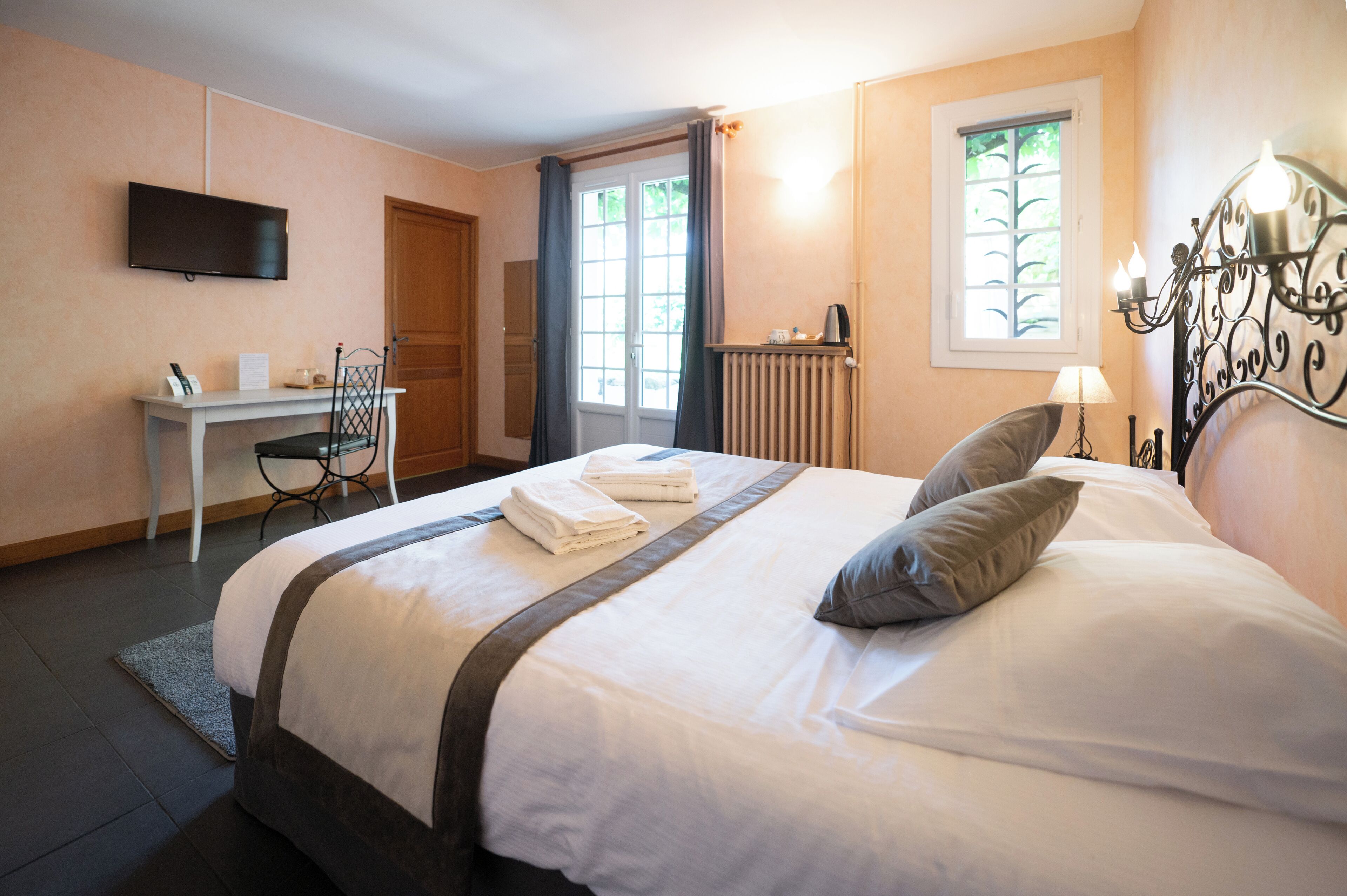 Una habitación de hotel ordenada con cama, escritorio, silla, televisor y ventana con cortinas.