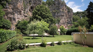 Un jardín con césped, árboles y una formación rocosa al fondo.