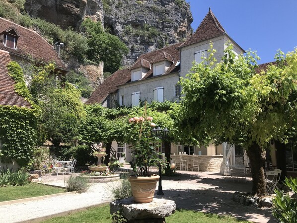 Un patio con una fuente de piedra, plantas en macetas y mobiliario de exterior.