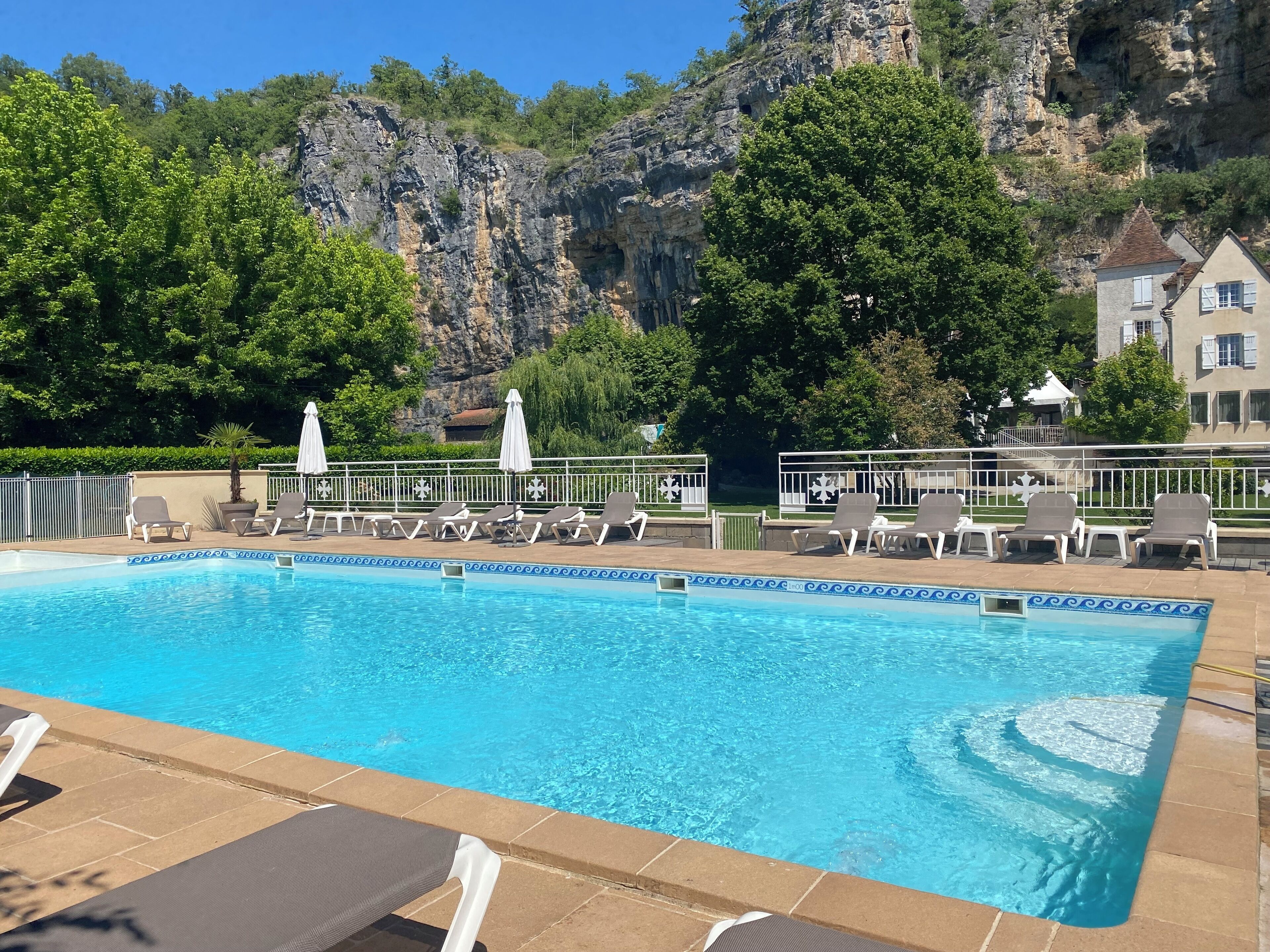 A swimming pool with lounge chairs and umbrellas, surrounded by greenery and a rocky cliff.