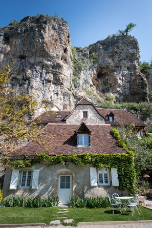 Una casa de piedra con techo de tejas, una puerta principal y un pequeño jardín con un banco.