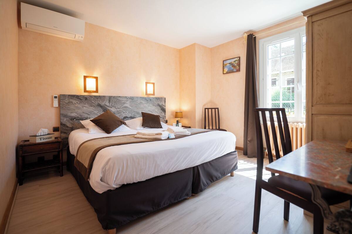A hotel room with a large bed, bedside tables, a small table, and a chair.