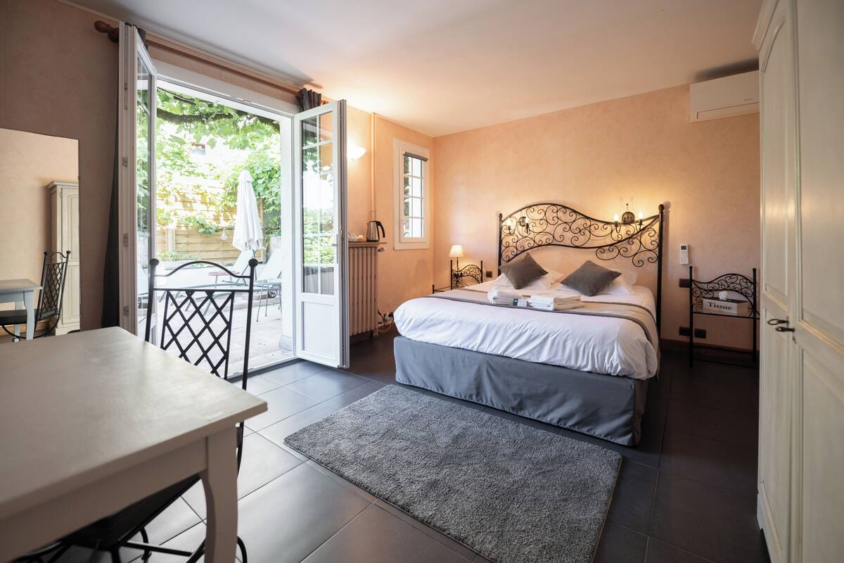 A bedroom with a bed, bedside table, and a view of the garden through an open door.