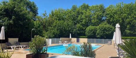 Una piscina con sillas de descanso y sombrillas, rodeada de vegetación.
