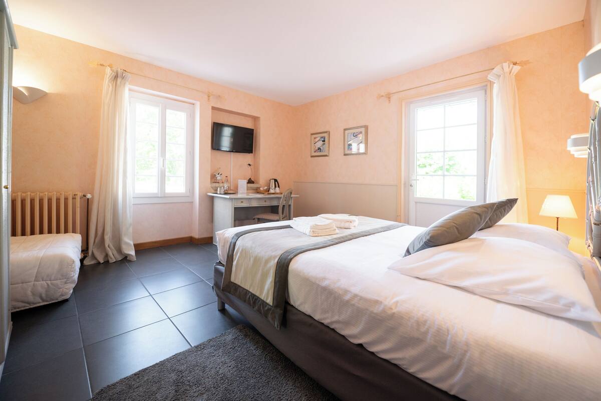 A bedroom with a bed, a desk, a chair, a radiator, and a TV on the wall.