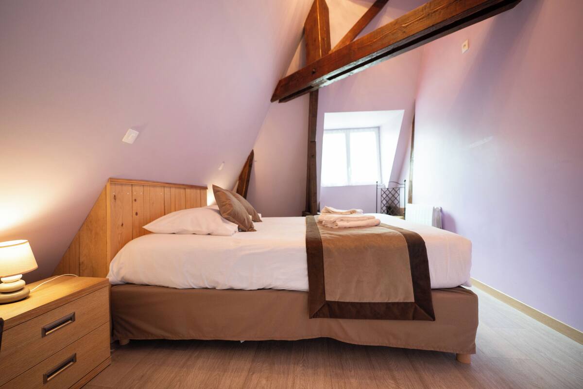 A bedroom with a wooden headboard, a bed with white linens, a brown throw blanket, and a nightstand with a lamp.