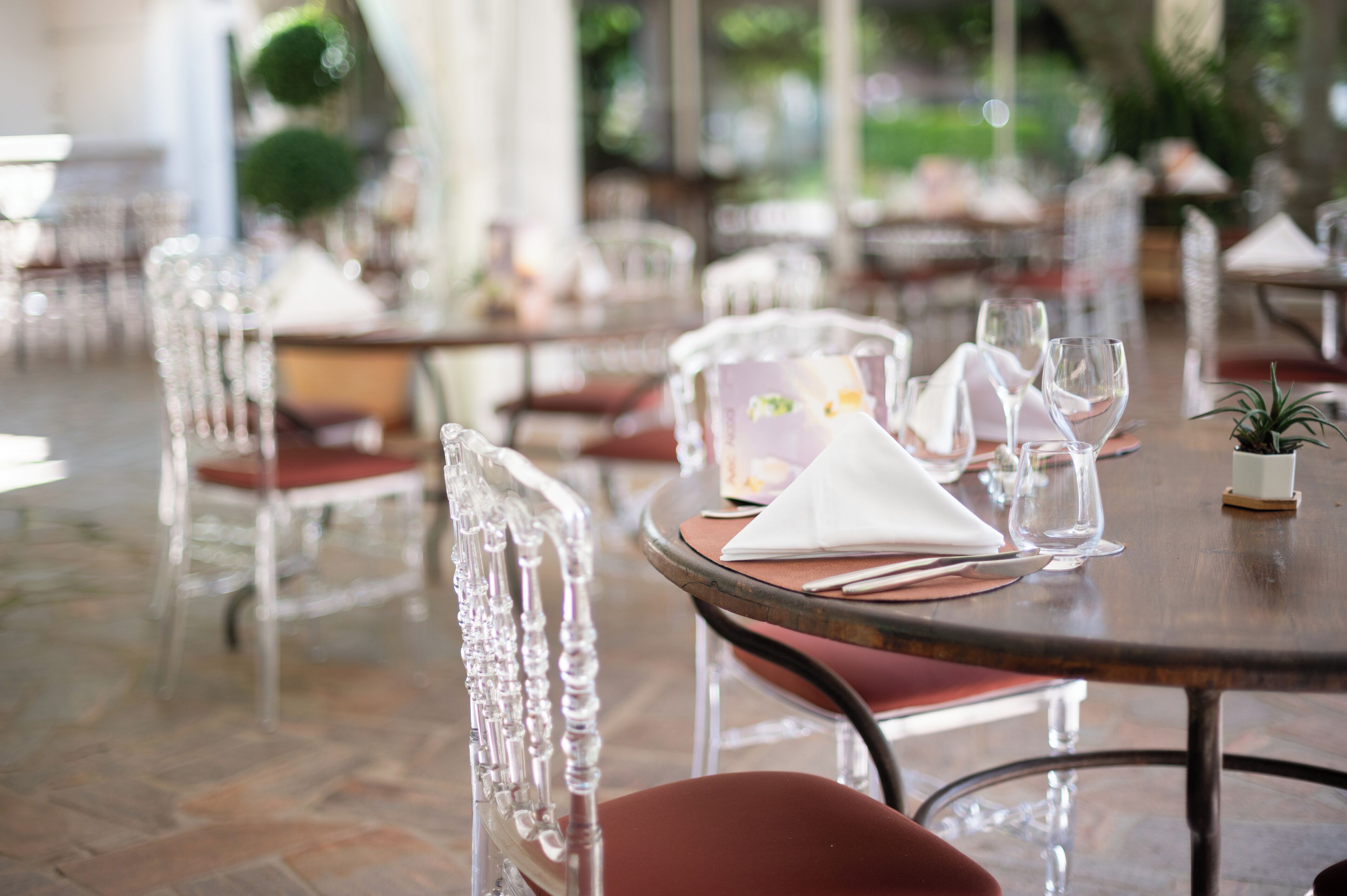 A restaurant with clear glass chairs and tables, arranged in a spacious indoor setting with a stone floor.
